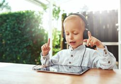 Blond boy using headphones and choosing music or show on digital tablet
