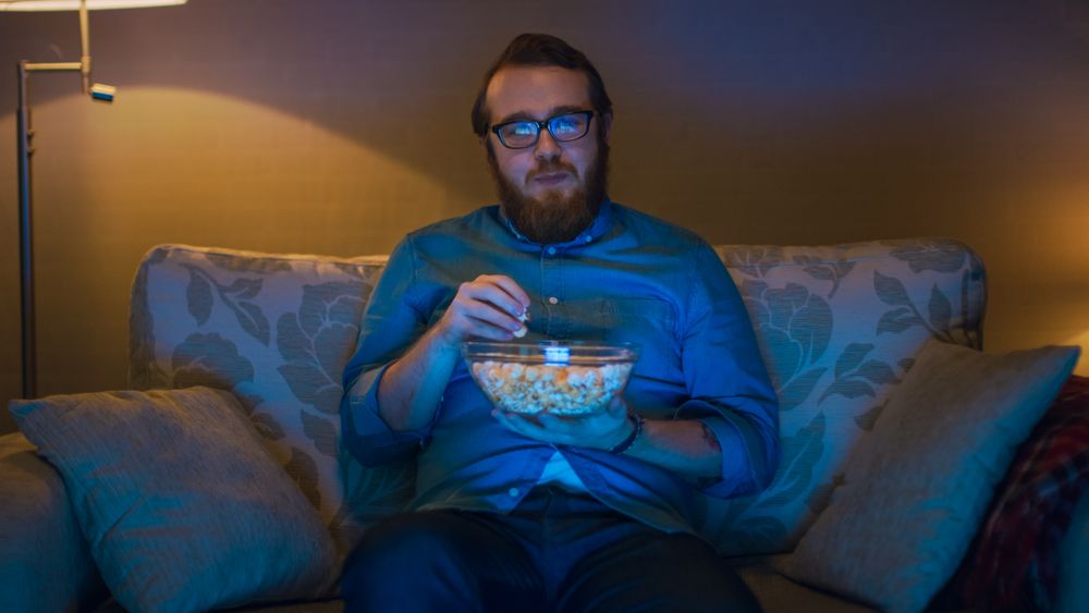 Portrait Shot of a Man Sitting on a Sofa in His Living Room, Eating Popcorn and Watching TV.
