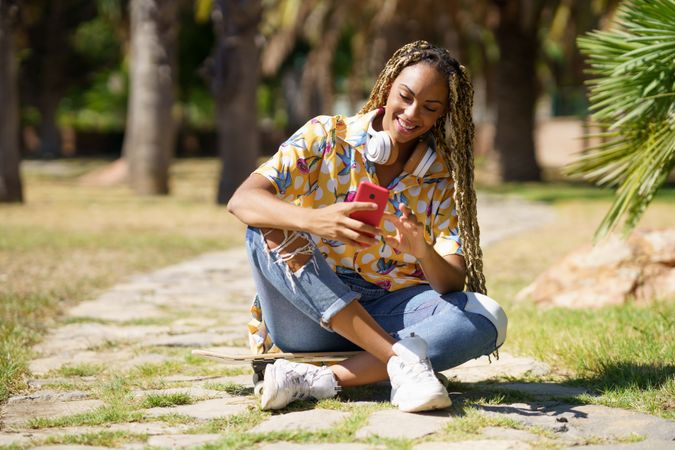Happy female in bold patterned shirt texting on phone in park
