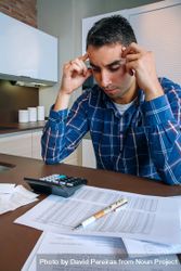Stressed man with calculator and bills in kitchen, vertical bevo60