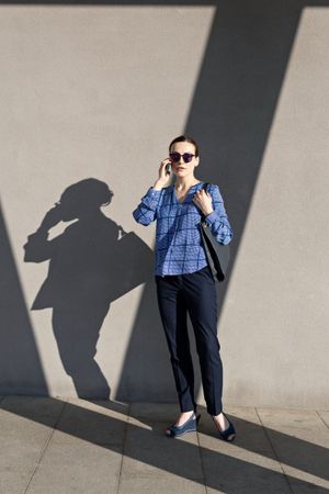 Businesswoman having smartphone conversation near gray wall