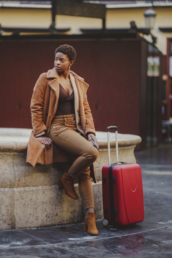 Woman sitting outside with chic red roller suitcase