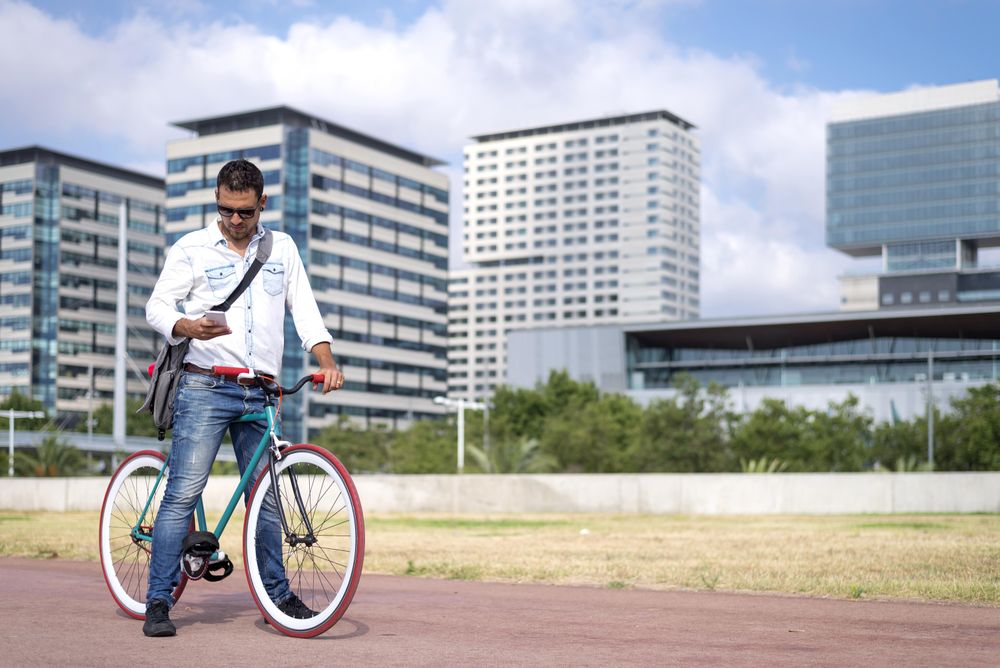 Male with colorful bicycle checking phone on city bike path