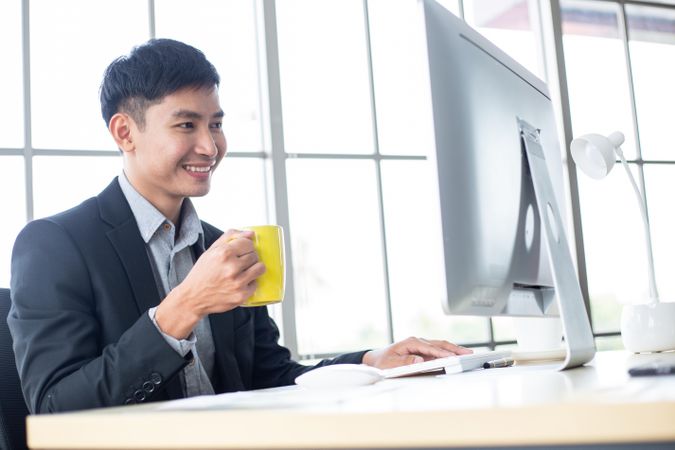 Businessman smiling looking at screen in the office with yellow mug