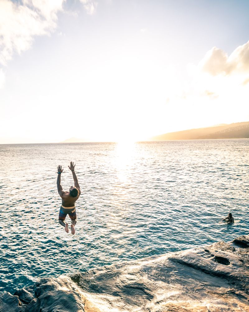 Man jumping into the sea while another man swimming