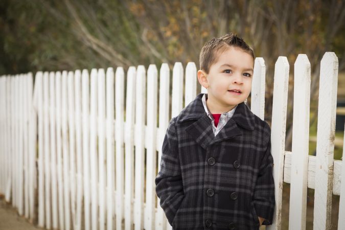 Young Boy Waiting For School Bus Along Fence Outside.
