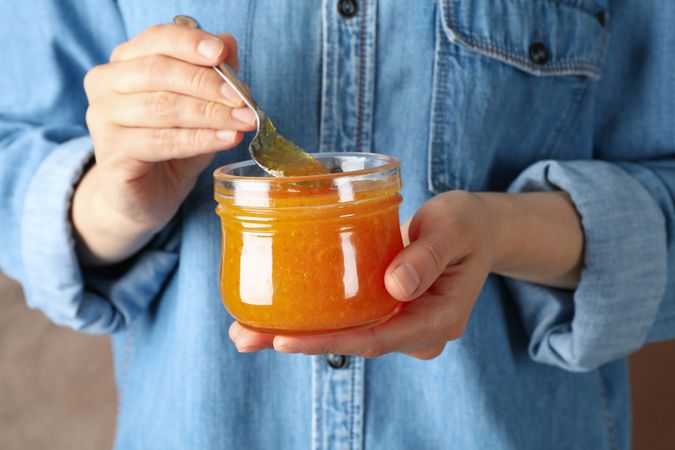 Woman holds glass jar with orange jam, close up