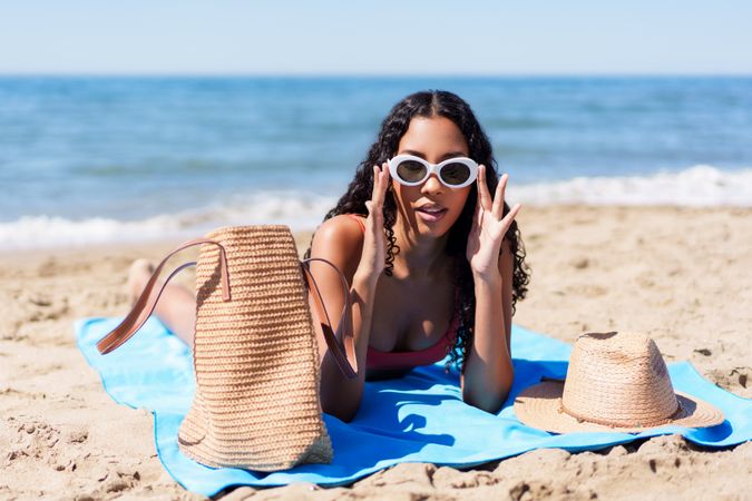 A Young Woman is Relaxing on the Beach, Wearing Stylish Sunglasses and Carrying a Beach Bag