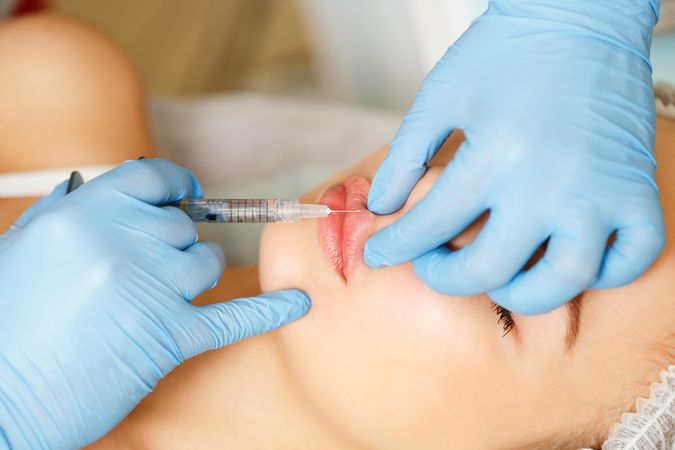 Hands in latex gloves injecting beauty treatment into lips