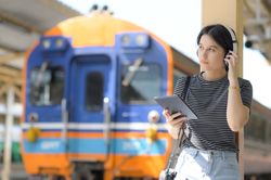 Young woman leaning on a pole at the train platform in headphones
