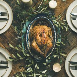 Centerpiece of roast chicken with decorative branches, with four plate settings, square crop