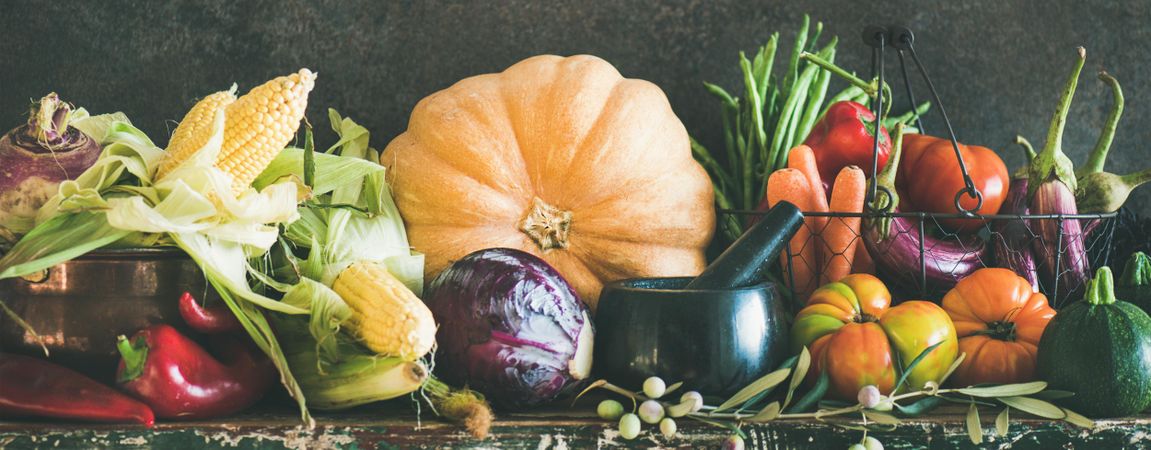 Fresh produce on counter with dark background with central squash, corn, cabbage, heirloom tomatoes