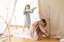 Happy little girls playing with sticks on wooden floor by white curtain