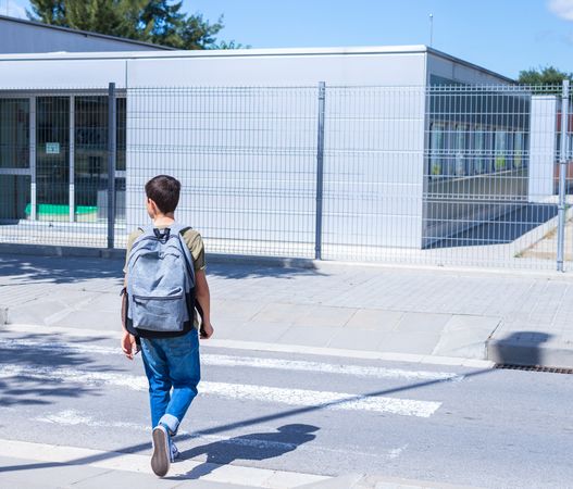 Boy crossing street wearing backpack on way to school