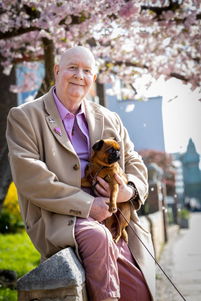 Smiling mature man sitting on wall near river holding dog