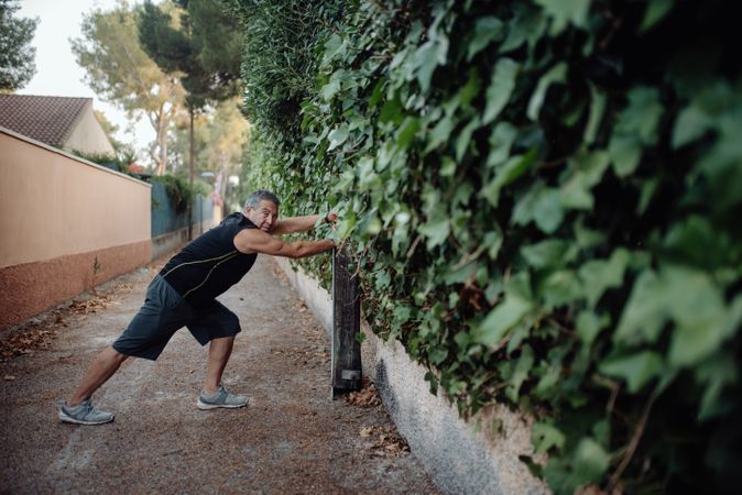 Mature man stretching on botanical wall in street