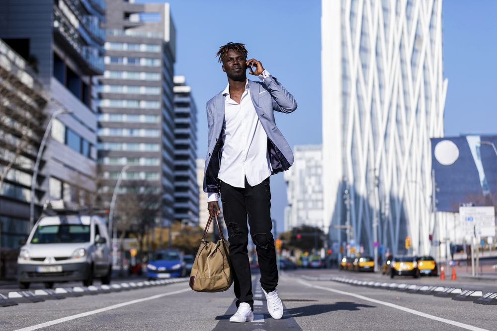Black man in elegant suit walking in the street while talking on his phone out on a sunny day