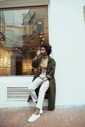 Black woman in green jacket drinking coffee outdoor