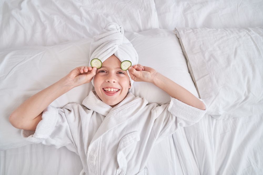 Boy taking off cucumber slices from eyes during spa procedures