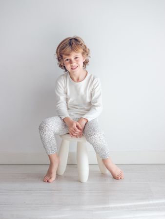 Boy in white pajamas leaning against the white wall of his house.