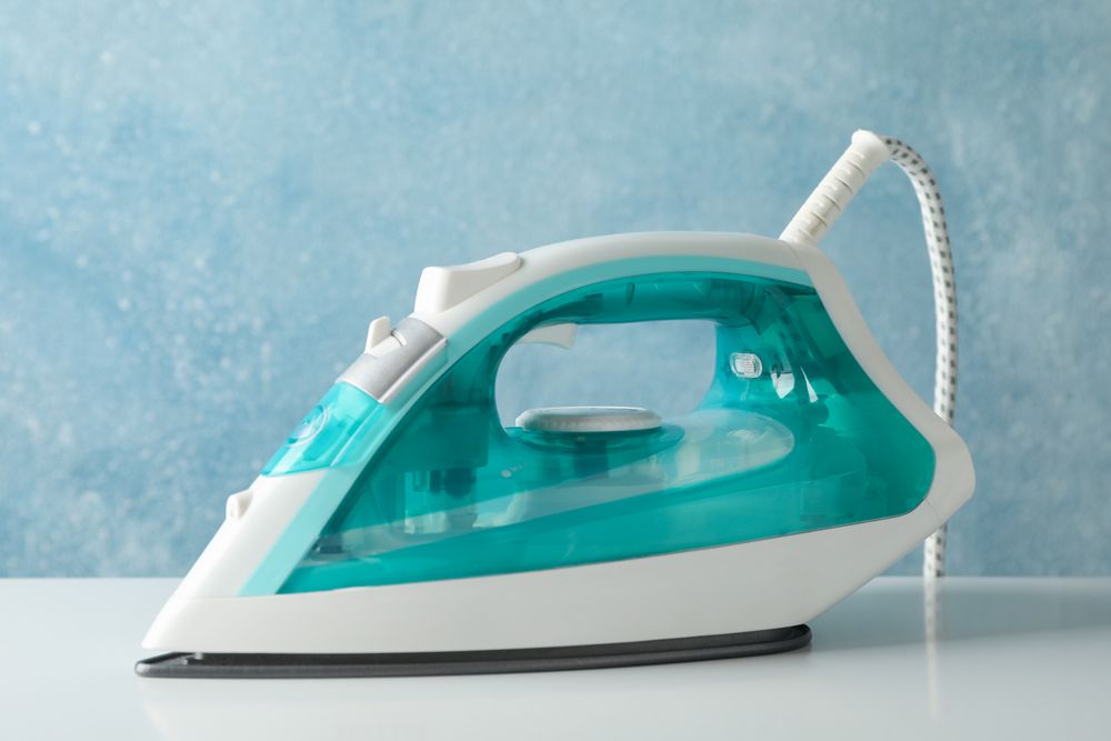 Iron on blank table against blue background, close up