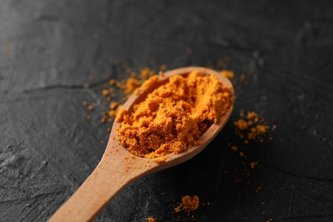 Looking down at wooden spoon of colorful turmeric, close up
