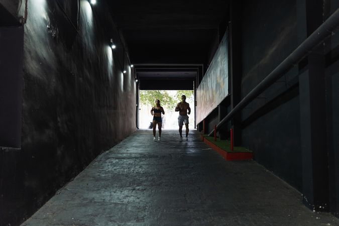 Unrecognizable sportive couple running in passage