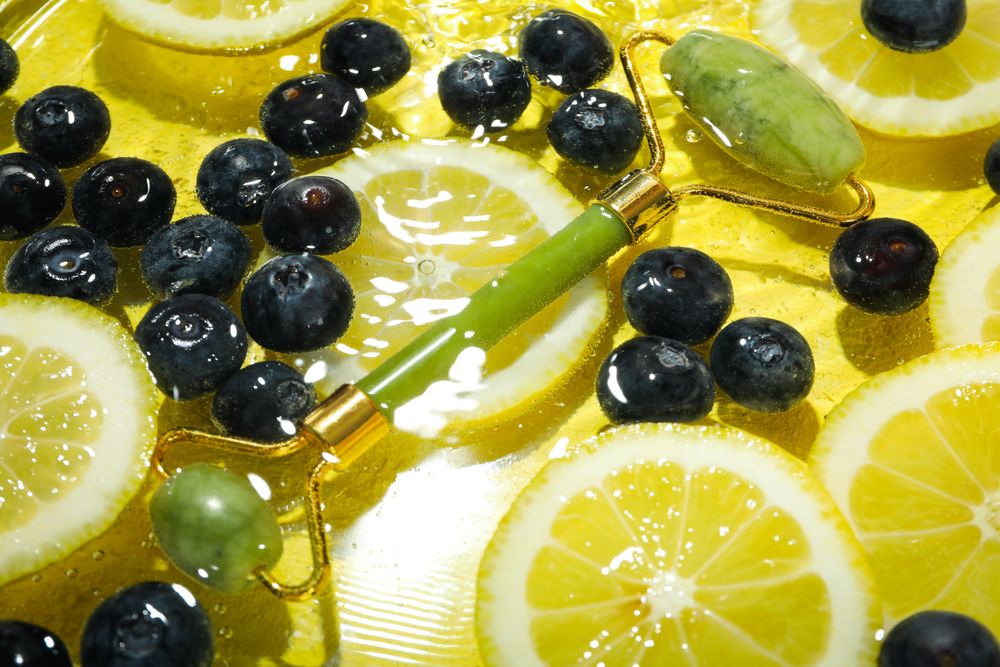 Top view of blueberries and lemons soaking in water with green jade roller