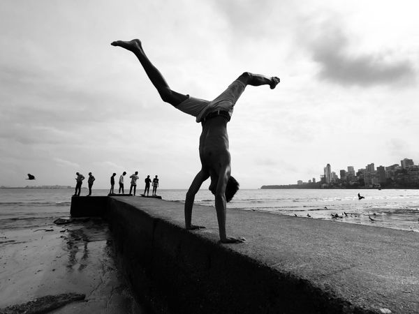 Grayscale photo of boy standing on his hands on seashore