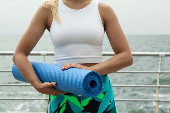 Woman with yoga mat in hands at sea