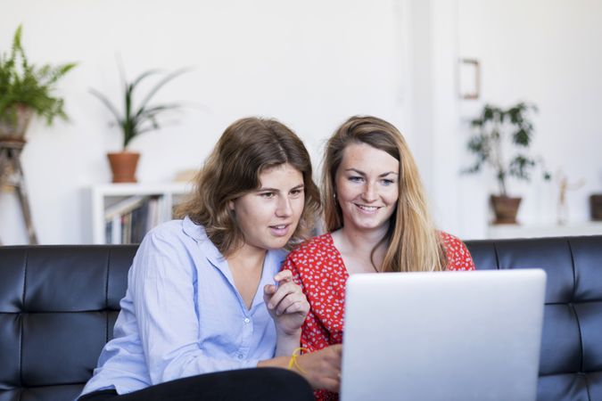 Two young women using computer while sitting on couch