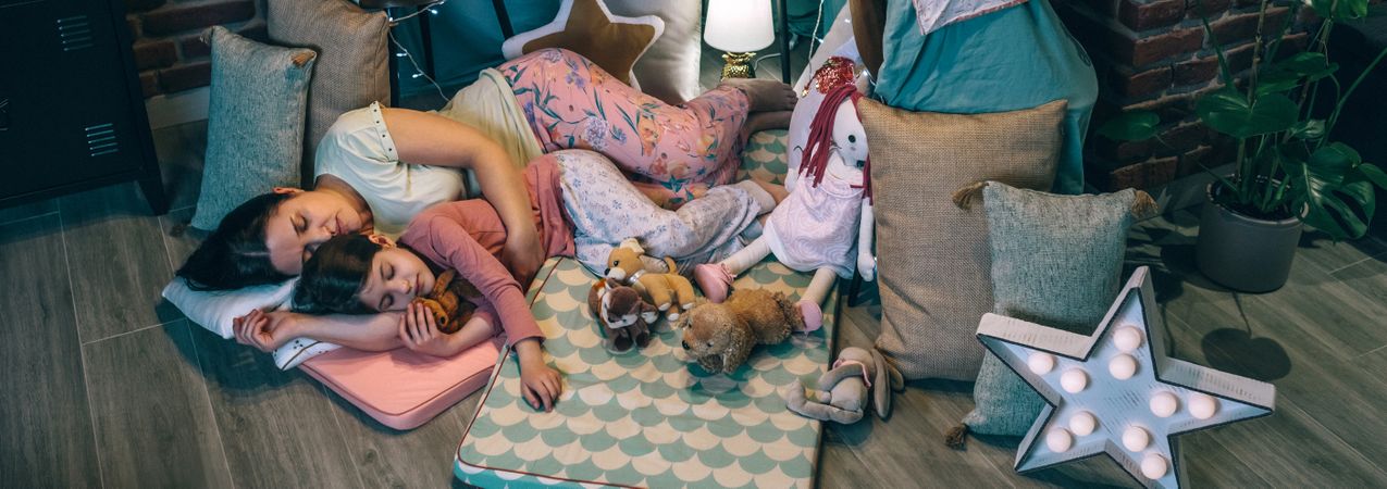 Banner of mother and daughter sleeping together lying over mats in cosy diy tent. Serene atmosphere.