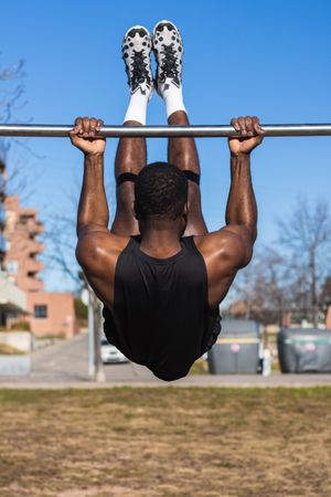 Unrecognizable strong Black sportsman working out on bar in town