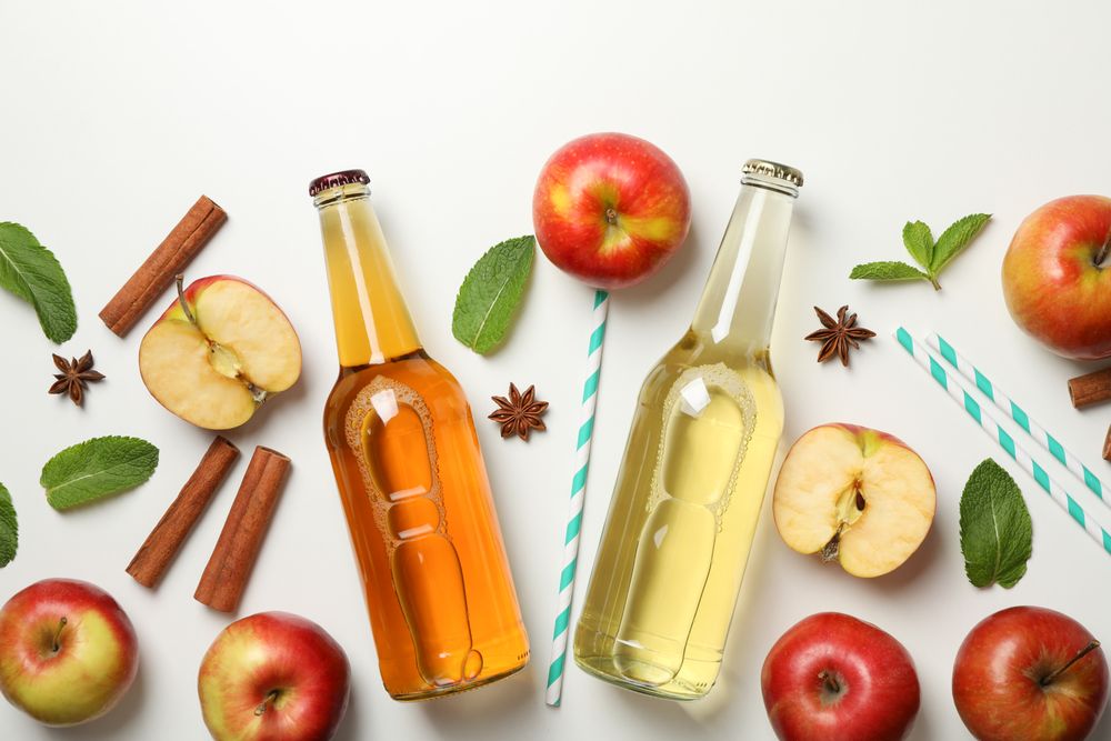 Composition with cider, apples, straws and cinnamon on light background