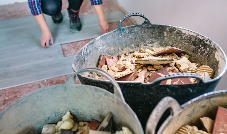 Construction rubble buckets with unrecognizable female bricklayer working in the background