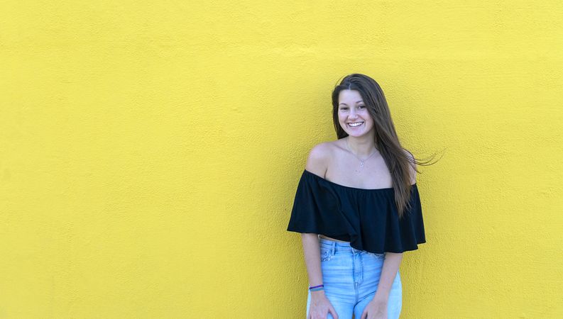 Beautiful woman leaning on yellow wall smiling on a sunny day