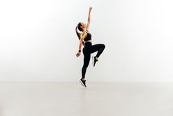 Woman jumping in the air against wall raising one hand up