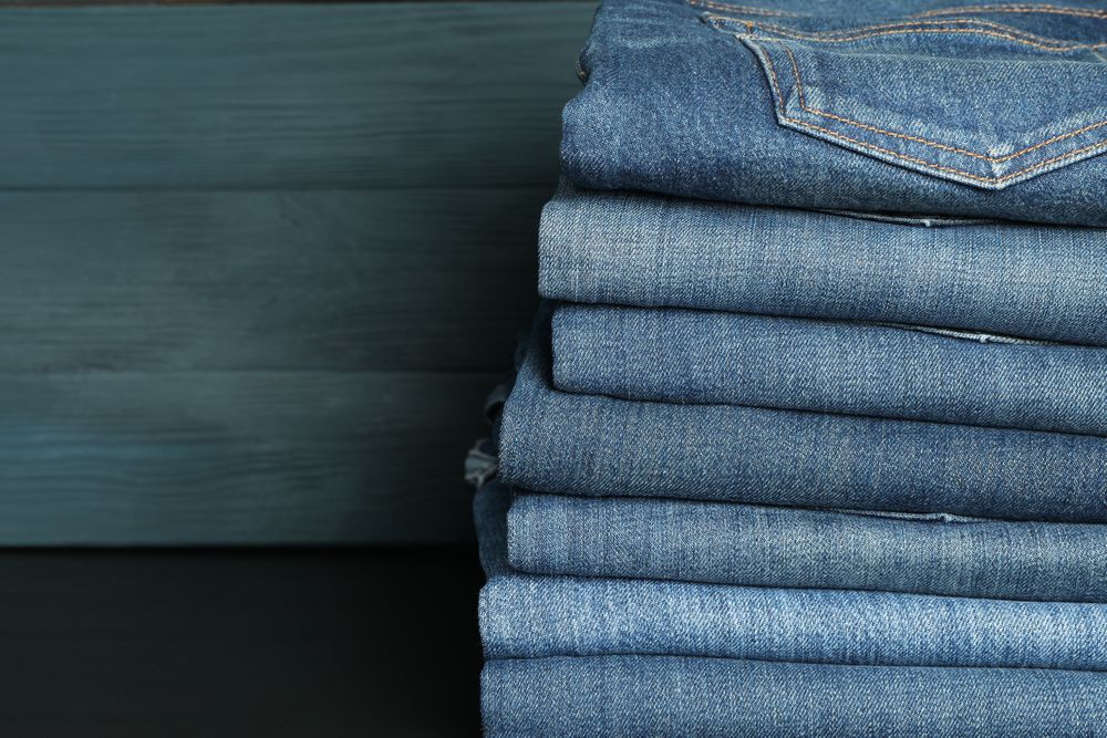 Stack of jeans pants on table, space for text