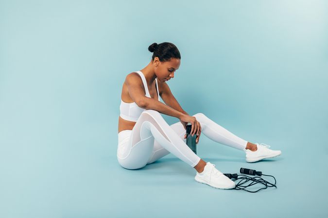 Fit Black woman sitting down in blue studio with water bottle and jump rope