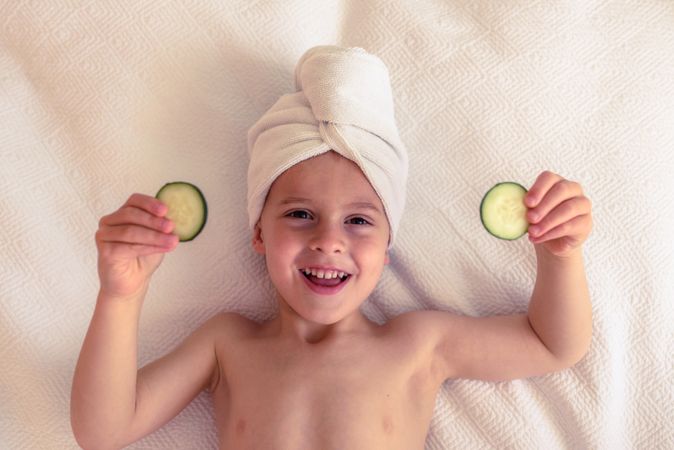Happy boy with towel on head and cucumber slices