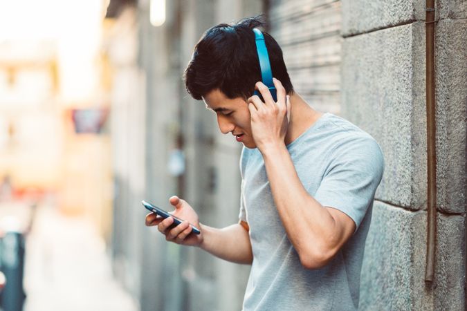 Content Asian man in headphones listening music on smartphone on street