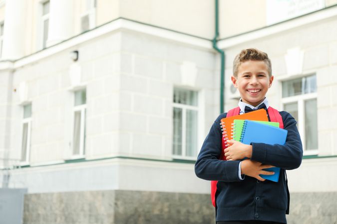 Boy with copybooks against school building, space for text
