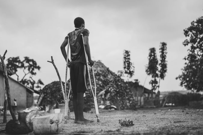 Back view of teenage boy walking with crutches outdoor in grayscale