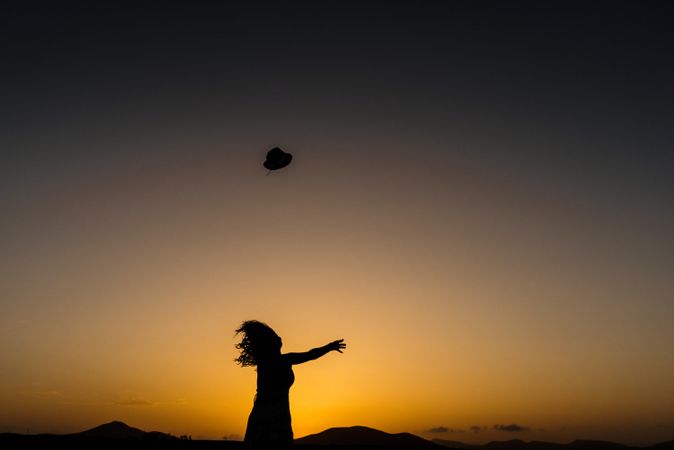 Woman throwing hat into distance to sun