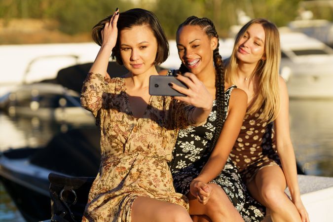 Three women sitting on wharf taking selfie