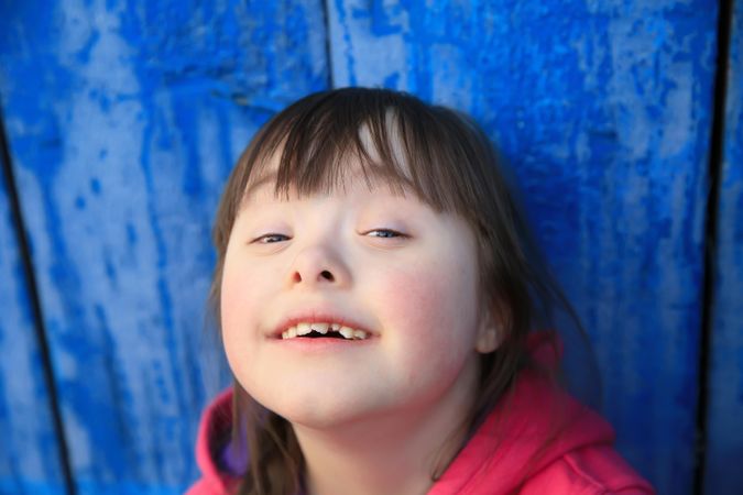 Young girl with a disability smiling against a blue wall