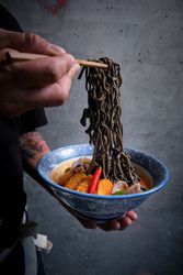 Male hand picking up noodles in a bowl of hot ramen with fish broth, squid, chilli, clams.