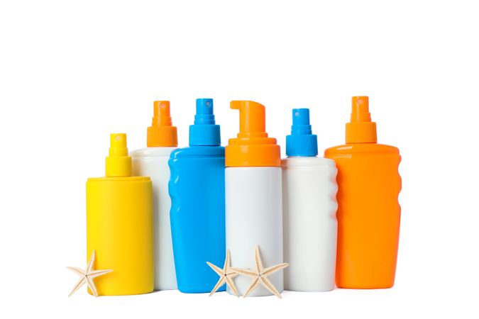 Many different sunscreen sprays with starfishes isolated on studio background. Summer vacation accessories