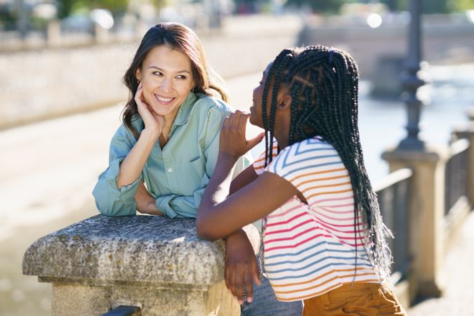 Female friends chatting while leaning on wall in casual clothing outside