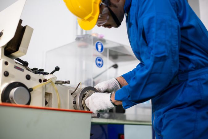 Male in blue jumpsuit and PPE gear operating machinery in manufacturing factory